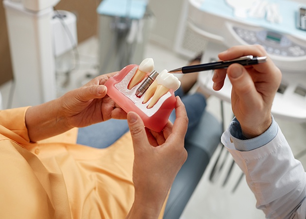 Dentist pointing to model of dental implant with pen