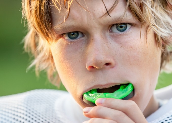 Young boy placing green athletic mouthguard into his mouth