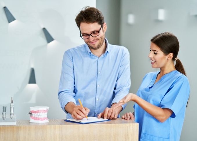 Dental team member showing a patient where to sign on a clipboard