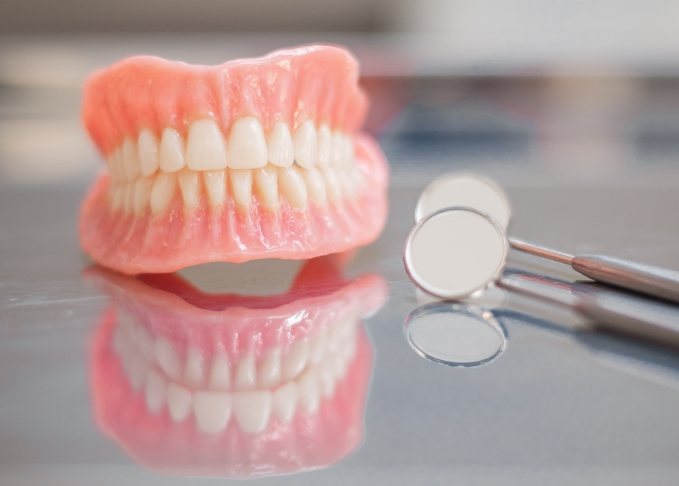 Full dentures on table next to two dental mirrors